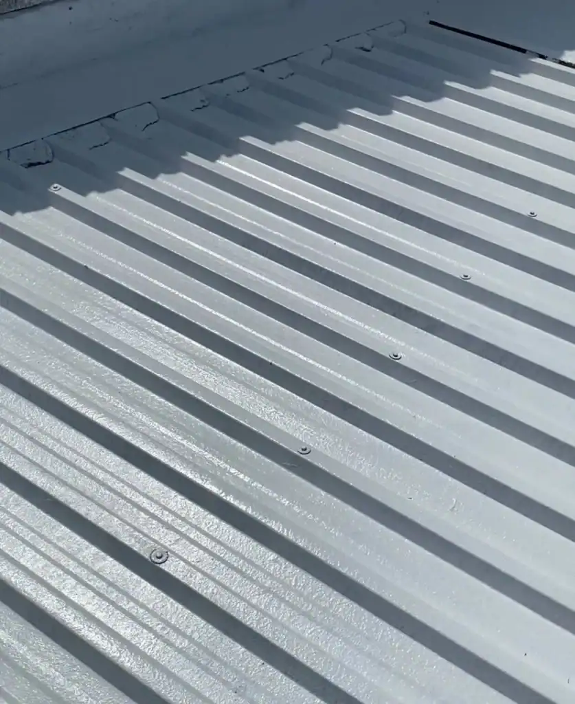 Close-up of silver metal roof panels with ridges and screws.